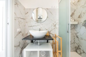 Un baño con un lavabo blanco, paredes de mármol y un espejo encima.