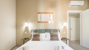 Ein Hotelzimmer mit einem Bett, zwei Nachttischen, einer Wand-Klimaanlage und einer Tür zu einem anderen Raum.