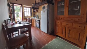 A kitchen with wooden cabinets, a dining table, chairs, a refrigerator, and a window.