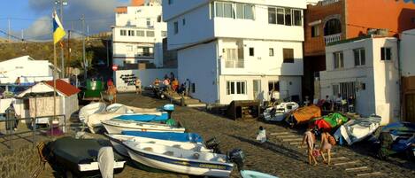 A coastal town with boats docked along the shore, buildings with balconies, and a clear sky.