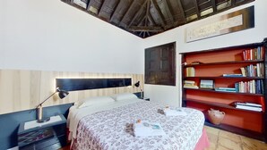A bedroom with a bed, bedside lamps, a wooden headboard, a bookshelf, and a decorative wall piece. - Remarkable 4-bed Villa (San Cristóbal de La Laguna)