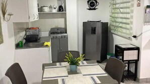 Een kleine keuken met een fornuis, koelkast en een eethoek met twee stoelen en een tafel.