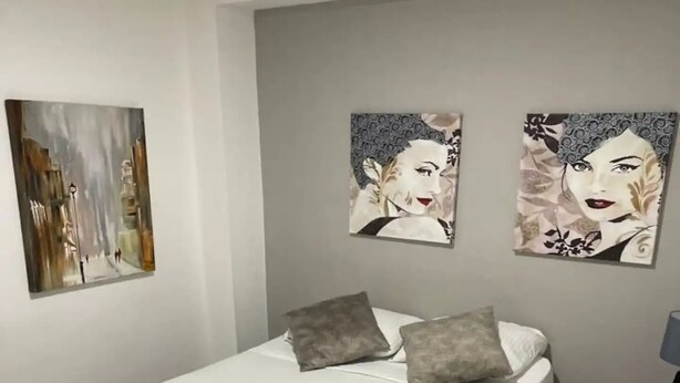 Een slaapkamer met een bed, kussens, een kussen in de vorm van een zwaan, een nachtkastje en twee wanddecoraties.