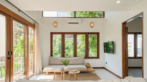 A spacious living room with a large sofa, wooden coffee table, and a TV mounted on the wall. - Treetop Villas (Pecatu)