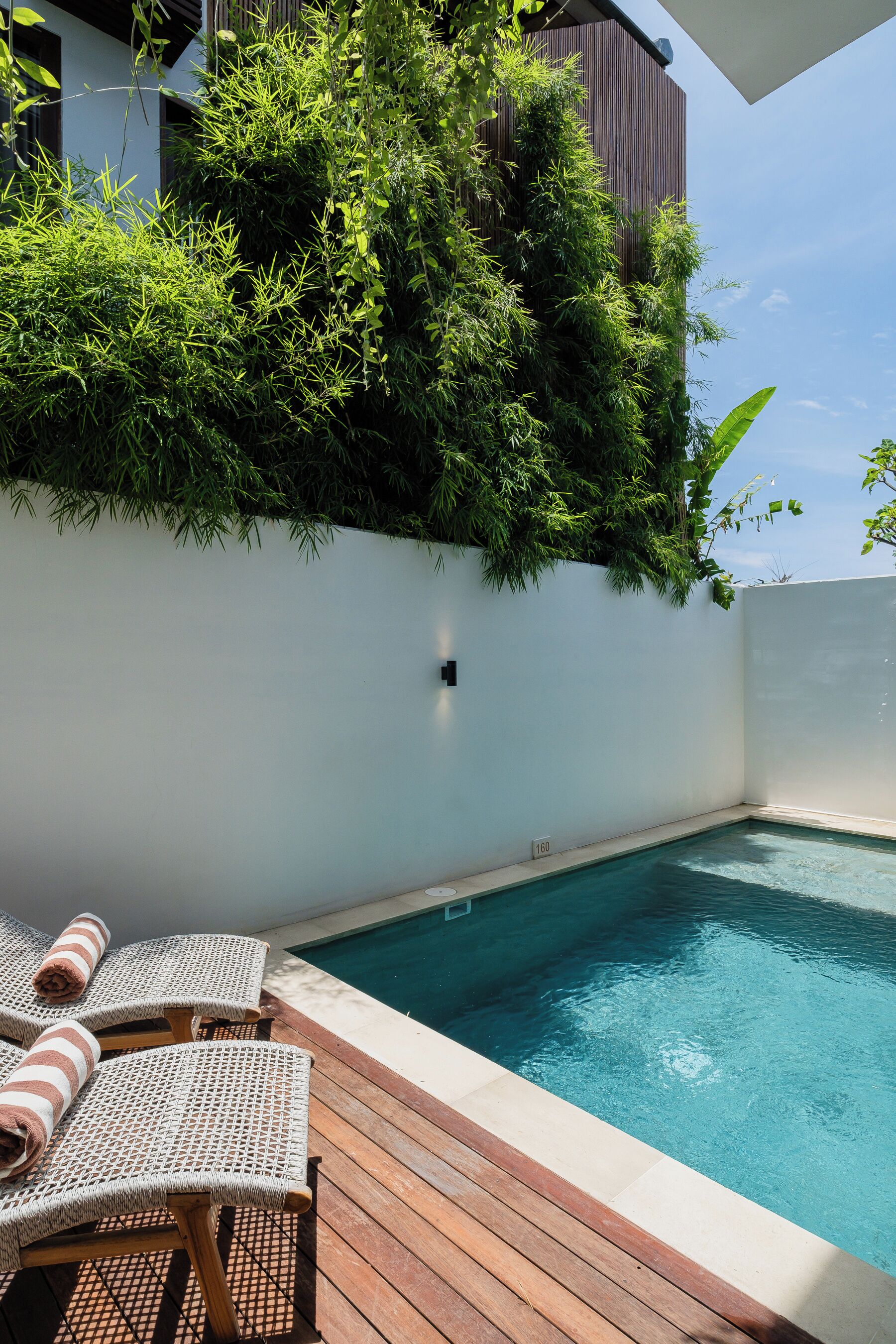 Un espace piscine doté d’une terrasse en bois, de deux chaises longues et d’un mur recouvert de verdure.