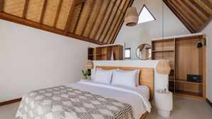 A bedroom with a high ceiling, wooden beams, a bed with a patterned bedspread, bedside tables with lamps, and built-in wooden shelving. - Treetop Villas (Pecatu)