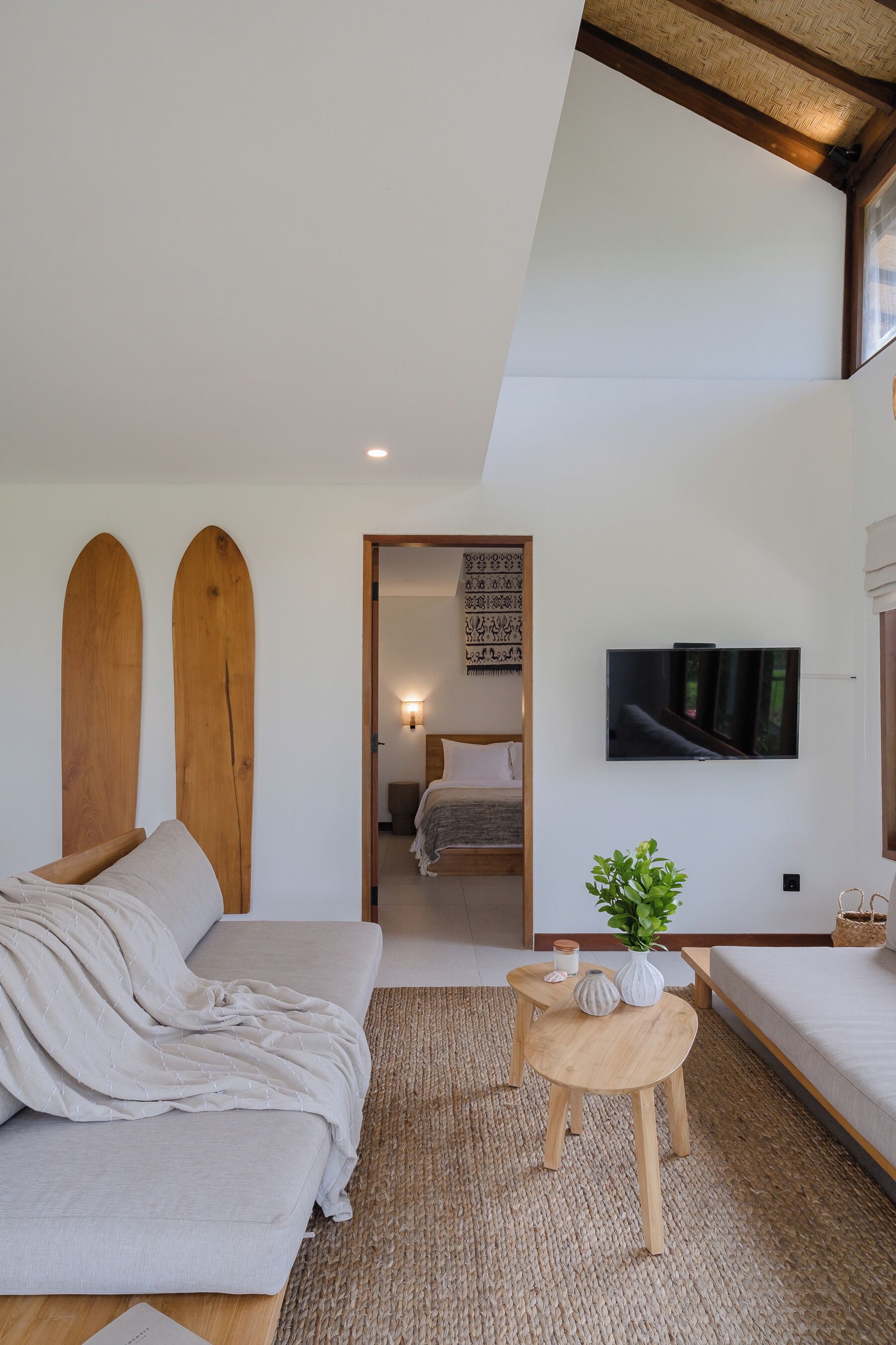 Un dormitorio moderno con un sofá, una pequeña mesa redonda con una planta y un televisor montado en la pared.