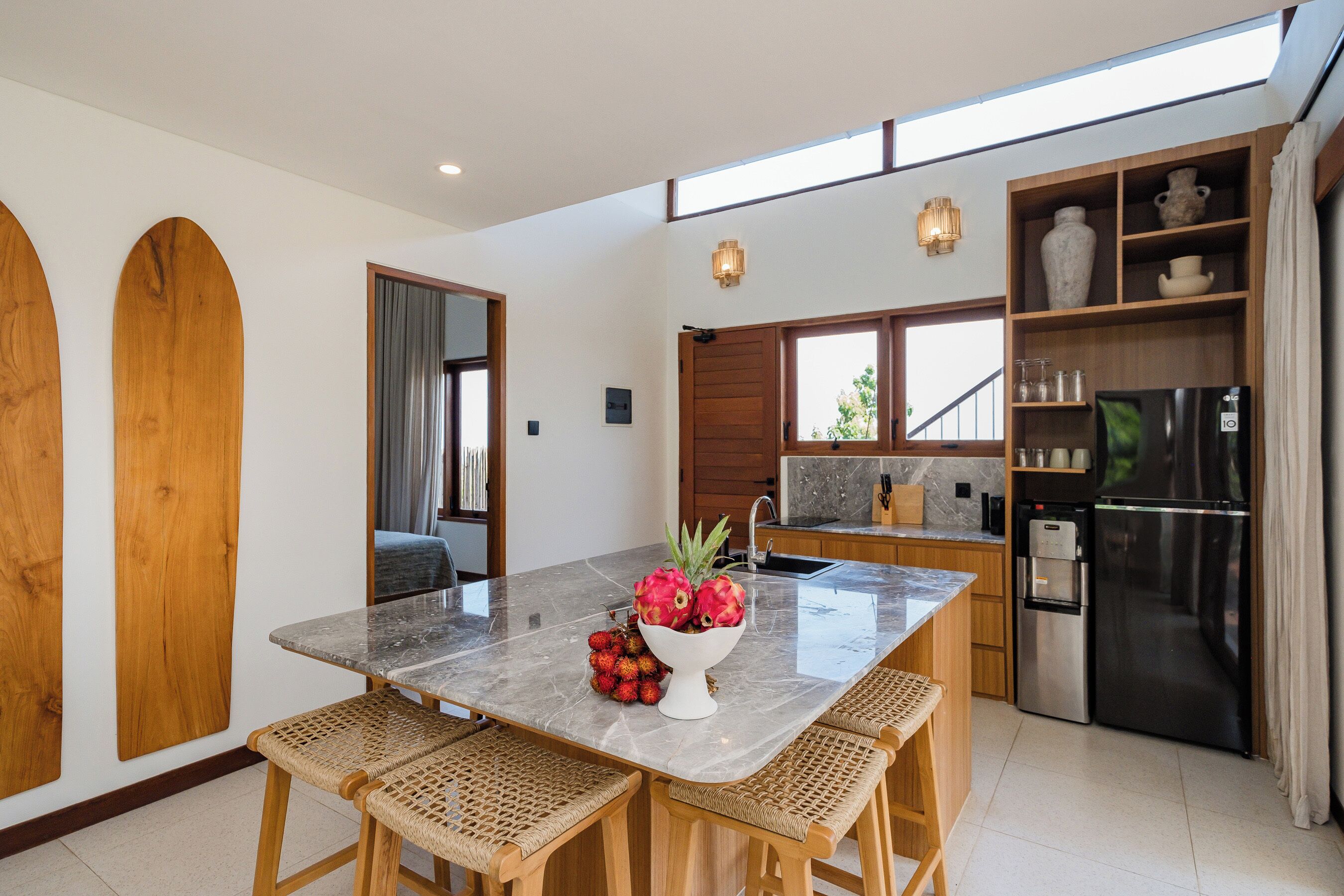 A modern kitchen with a marble countertop, wooden chairs, a fruit bowl, and a built-in refrigerator.
