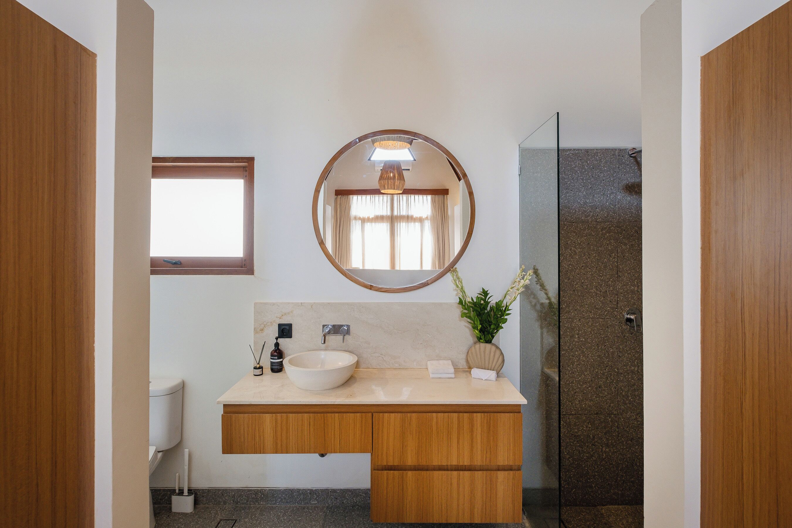 Un bany modern amb un mirall rodó, un lavabo independent, mobles de fusta i una cabina de dutxa de vidre.