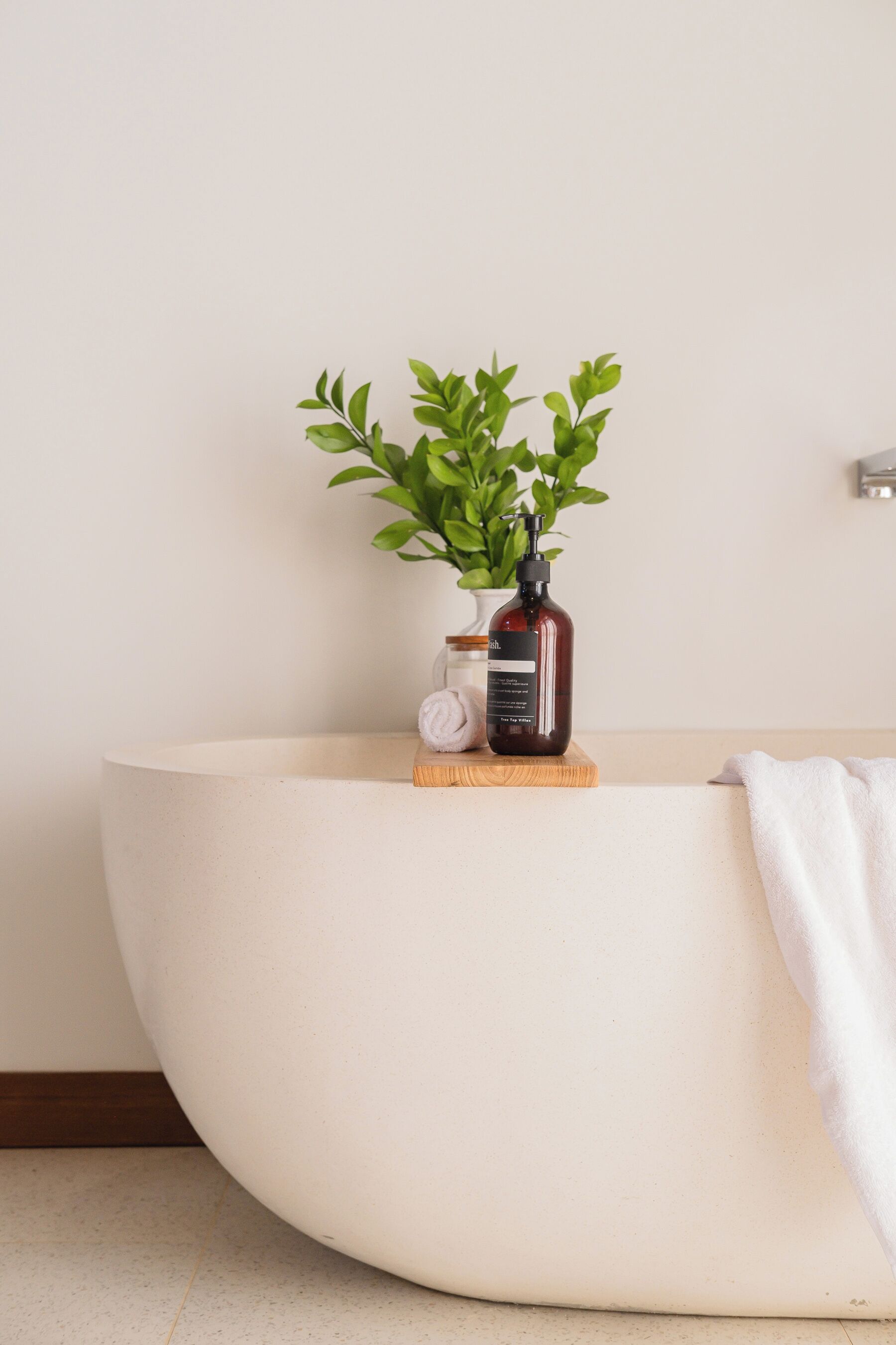 A bathroom with a white bathtub, a small potted plant, and a bottle of liquid soap on a wooden tray.