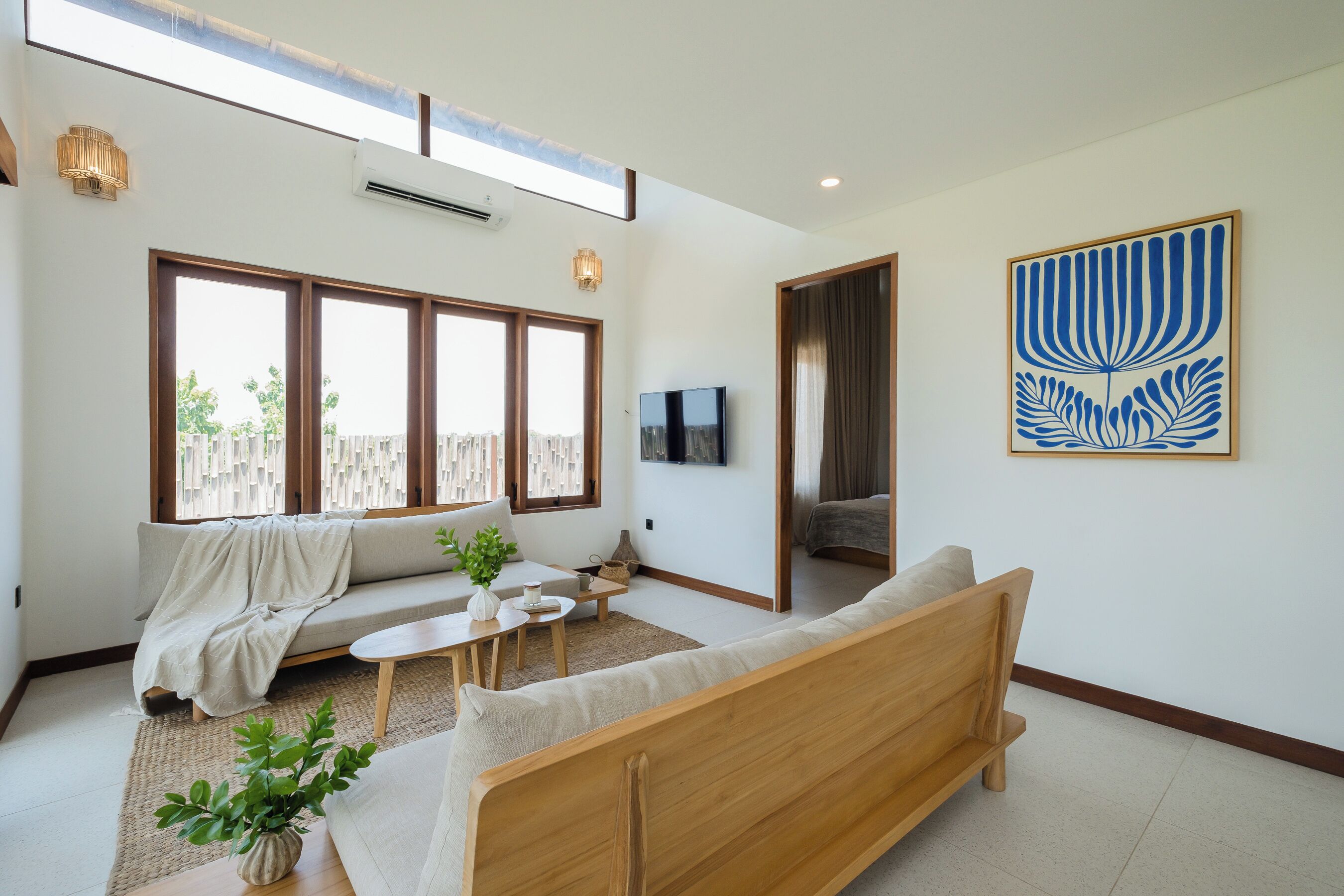 A modern living room with a sofa, coffee table, and TV. There are large windows and a ceiling fan.