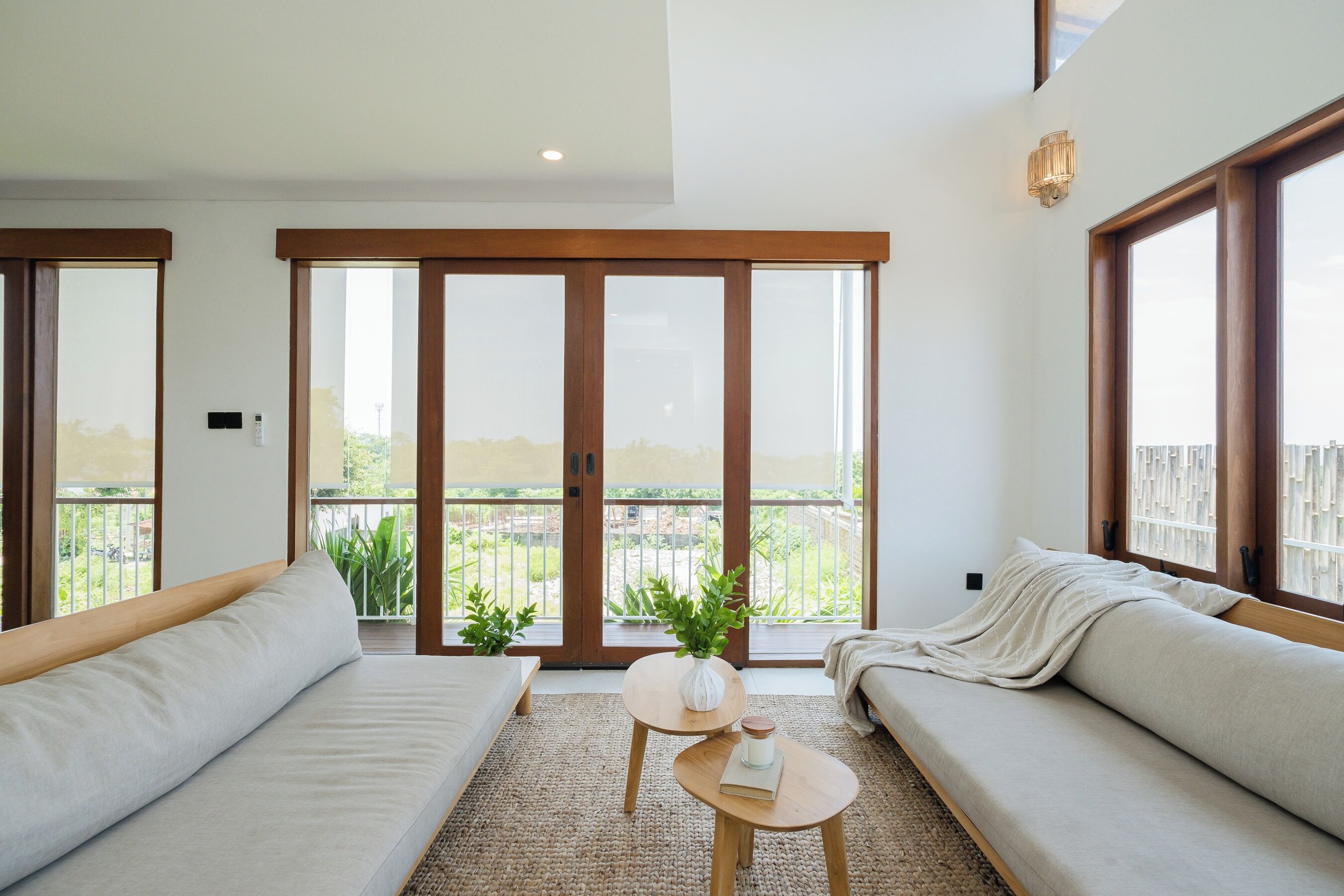 A modern living room with two sofas, a small round table, and a large sliding glass door leading to a balcony with plants.