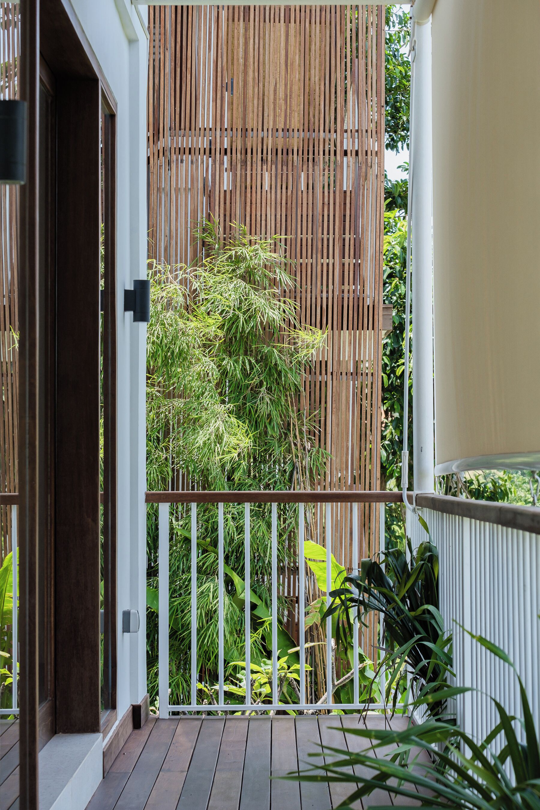 A wooden balcony with a white railing, a bamboo fence, and lush greenery in the background.
