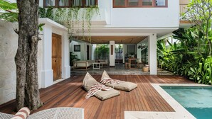 A modern outdoor living area with a wooden deck, lounge chairs, and a pool. - Treetop Villas (Pecatu)