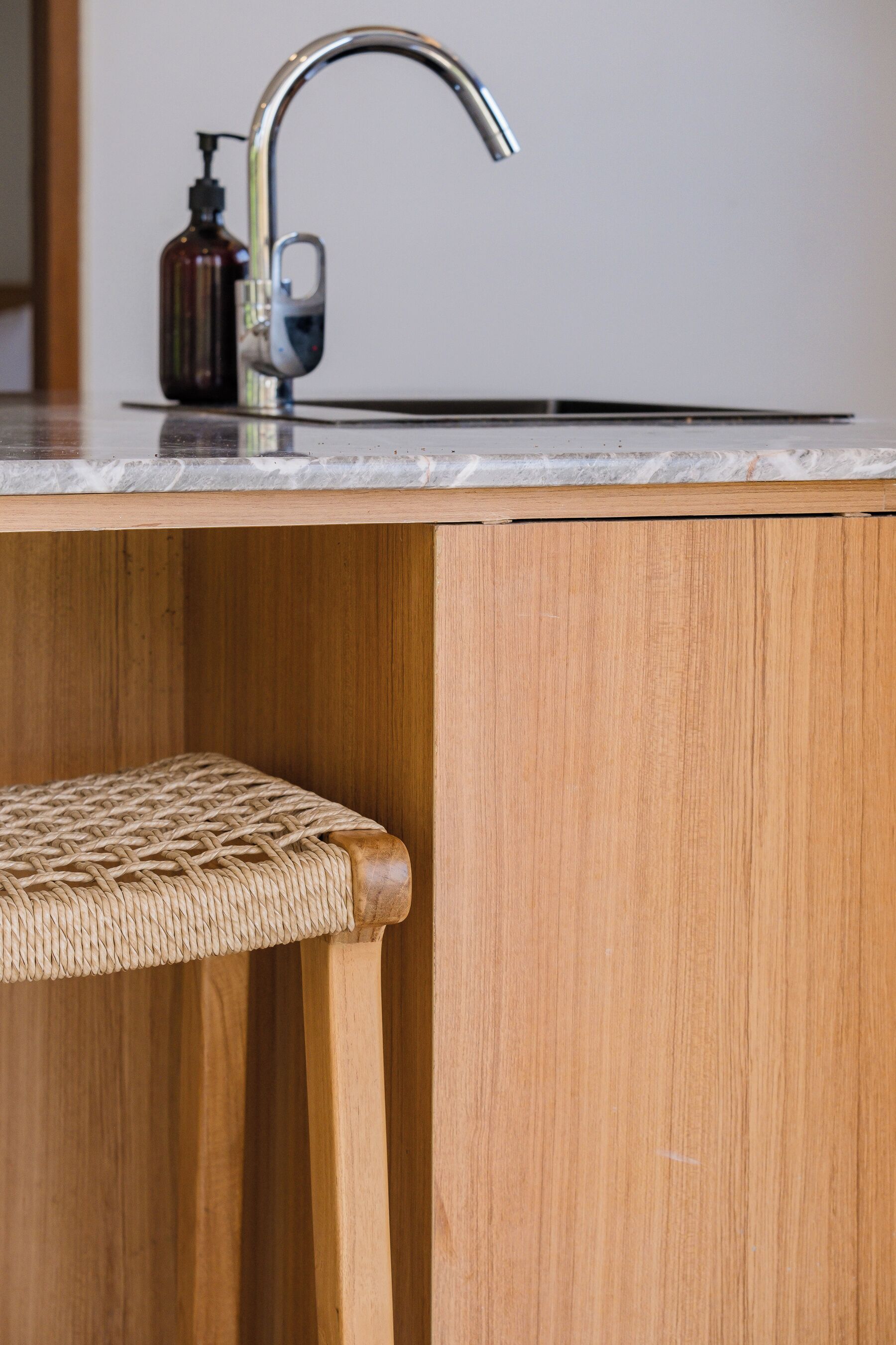 A kitchen counter with a stainless steel faucet, a soap dispenser, and a woven stool.