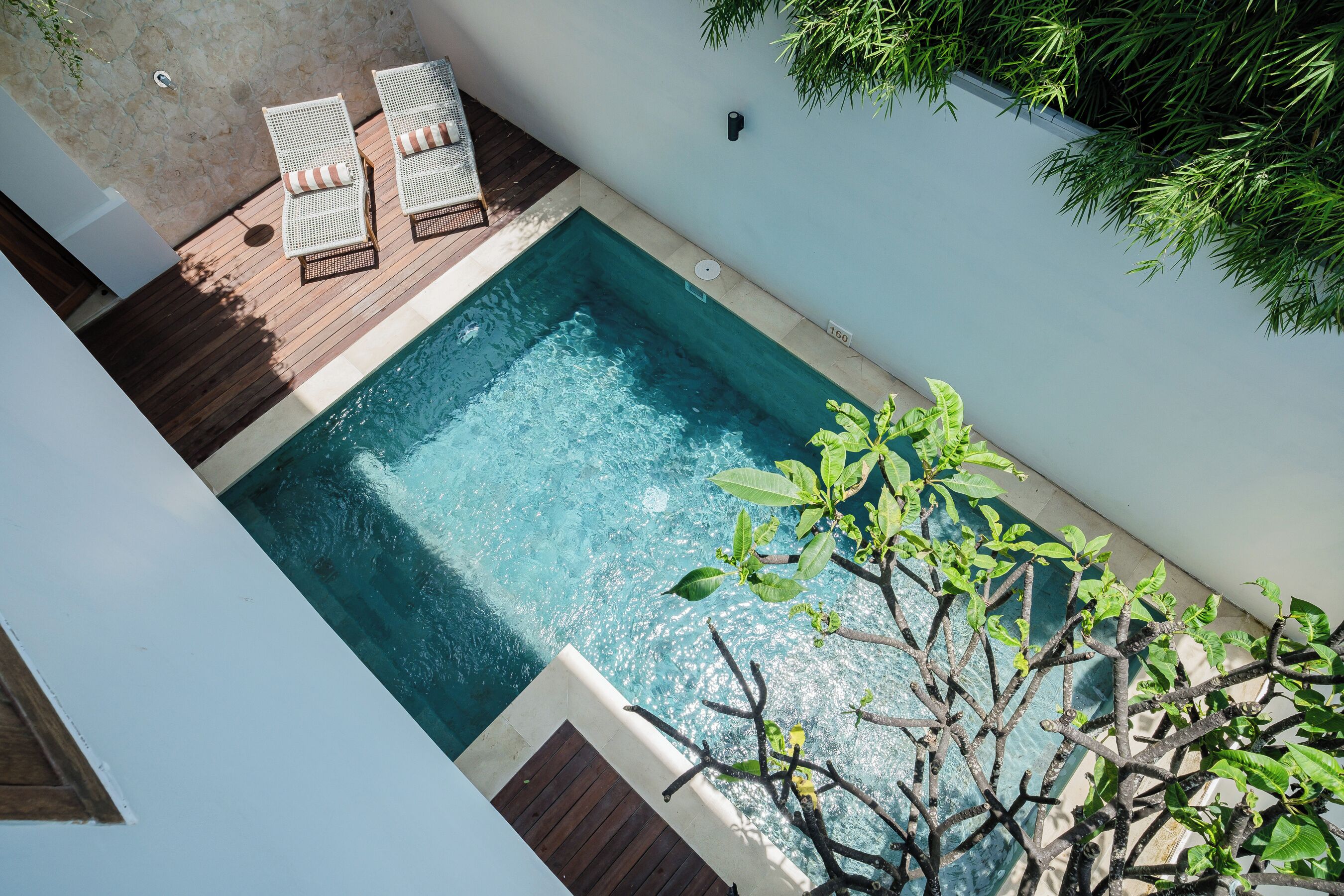 Une piscine rectangulaire avec deux chaises longues et un petit espace aménagé autour de la piscine.