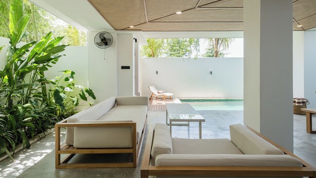 Zona relax esterna moderna con divani e un tavolo, immersa nel verde e con vista su una piscina.