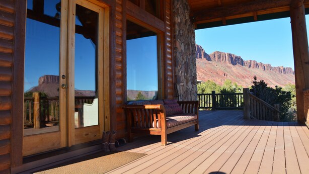 Un terrazza in legno con una panchina e un pilastro in pietra, con vista su un paesaggio montuoso.
