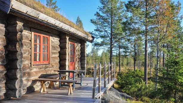 Eine rustikale Holzhütte mit einer Holzterrasse und einer roten Tür.