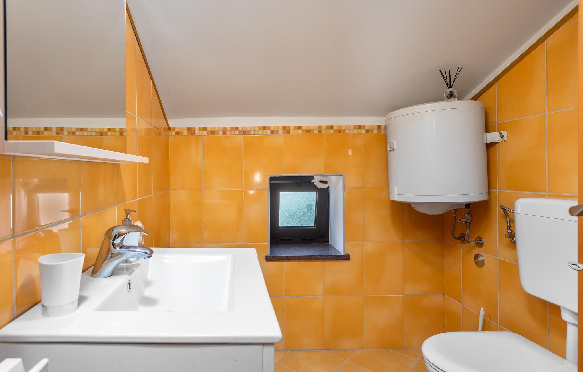 Un bagno con piastrelle arancioni, un lavandino bianco, uno specchio, un water e uno scaldabagno bianco.