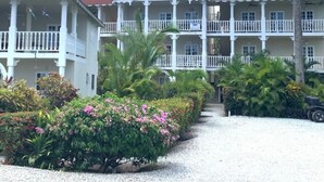 A multi-story building with balconies, surrounded by tropical plants and a gravel pathway. - PROMO Beachfront sunsets with Starlink WIFI (Las Terrenas)