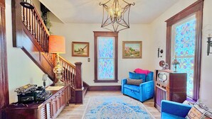 Ein geräumiges Wohnzimmer mit einer Holztreppe, einer Chandelüster, einem blauen Sessel und einem Vintage-Radio.