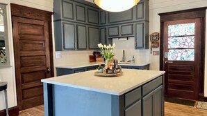 Eine Küche mit dunkelblauen Schränken, einer großen Kochinsel mit Blumenvase und einer Buntglas-Tür.