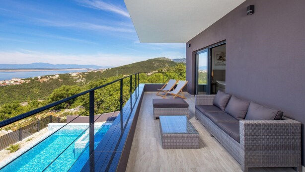Un balcon avec une piscine, des meubles en osier et une vue sur un paysage côtier.