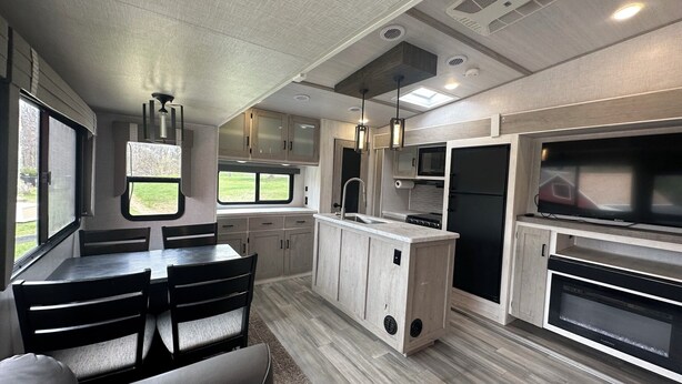 A modern RV kitchen with a dining area, built-in appliances, and a large TV. - Horn and Thistle Farm - Camper/RV in Abbottstown, Pennsylvania, United States (Abbottstown)