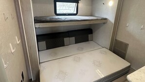 A compact RV interior with a bunk bed, a small window, and a kitchenette area. - Horn and Thistle Farm - Camper/RV in Abbottstown, Pennsylvania, United States (Abbottstown)