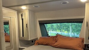 A bedroom with a large bed, a window with a view of trees, and a ceiling vent. - Horn and Thistle Farm - Camper/RV in Abbottstown, Pennsylvania, United States (Abbottstown)