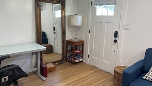 Una habitación con un escritorio blanco, una silla azul, una lámpara, un espejo y una puerta.