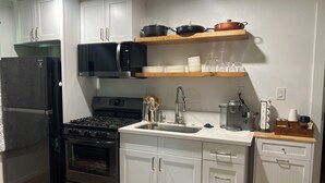 Una cocina compacta con armarios blancos, un refrigerador negro, una estufa y un microondas.