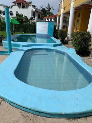 A swimming pool with a blue tiled deck, surrounded by greenery and buildings. - Bungalows Isla bonita (Rincón de Guayabitos)