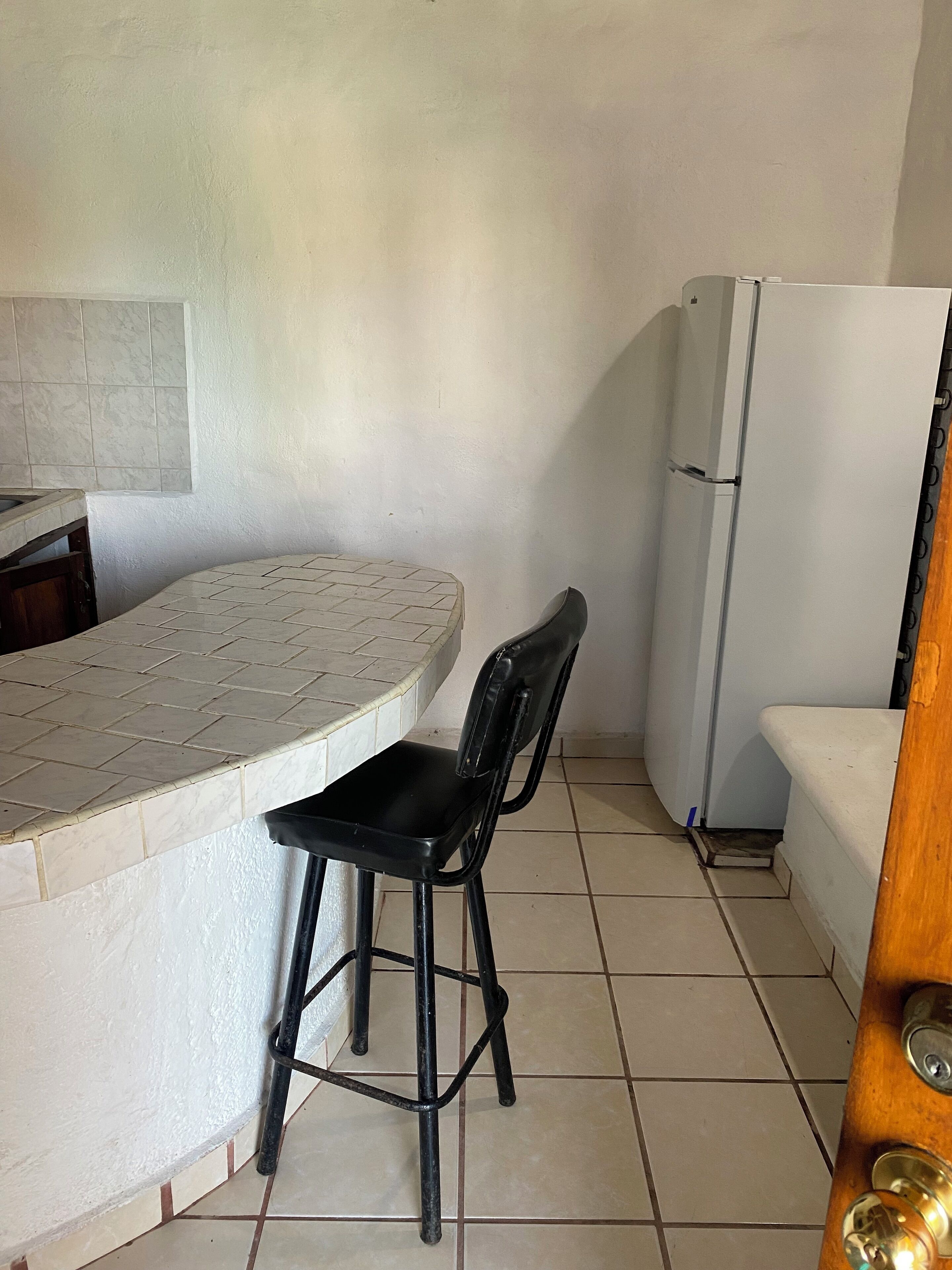A small kitchen with a white refrigerator, a tiled countertop, and a black chair.