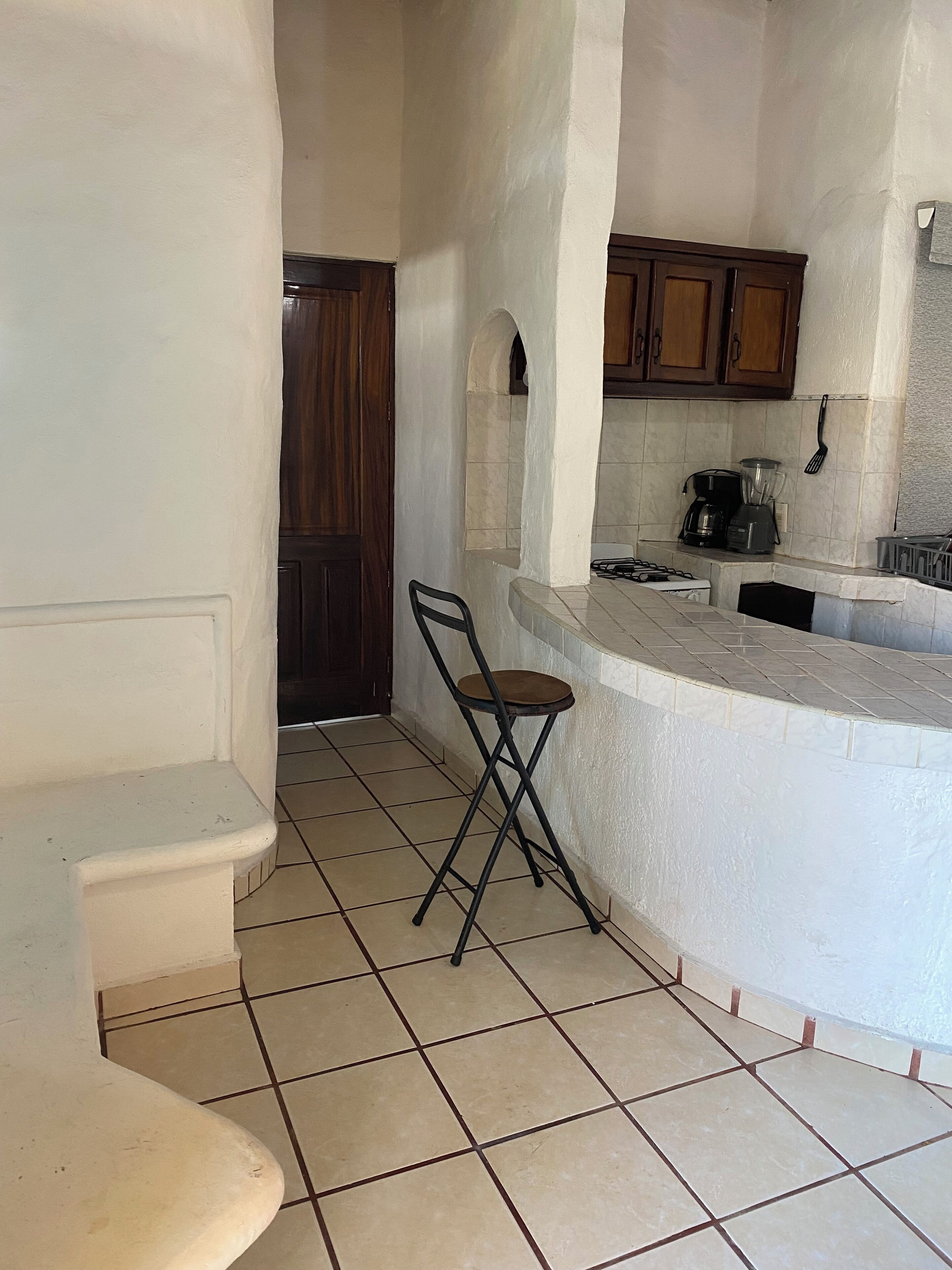 Una cocina con suelo de baldosas, una puerta de madera, una barra y una silla plegable.