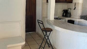 Una cocina con suelo de baldosas, una puerta de madera, una barra y una silla plegable.