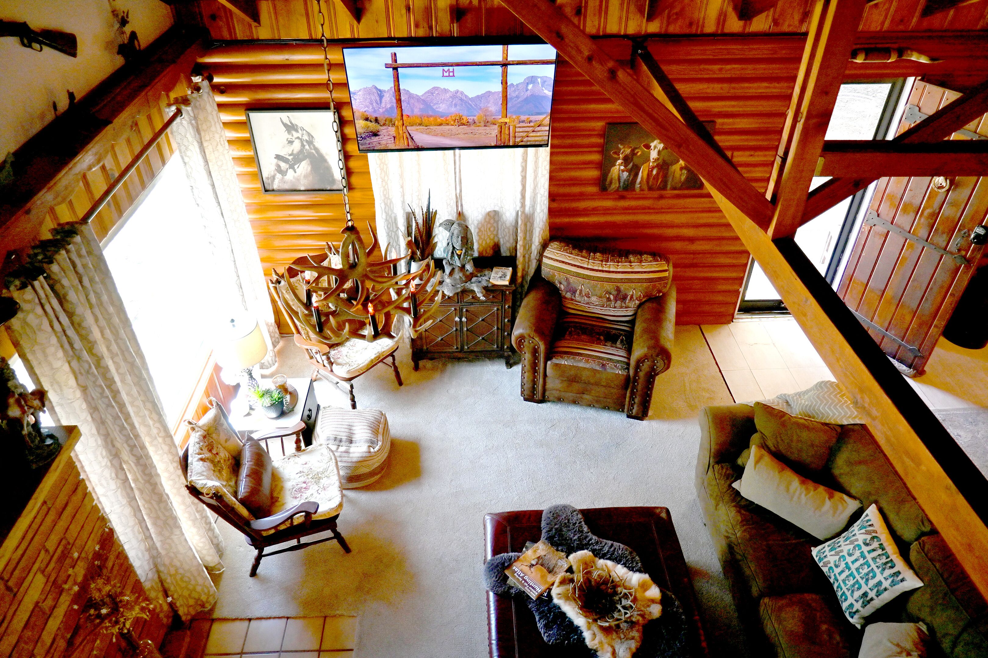 Un acogedor interior de cabaña con comedor, sofá y televisión mostrando un paisaje montañoso.