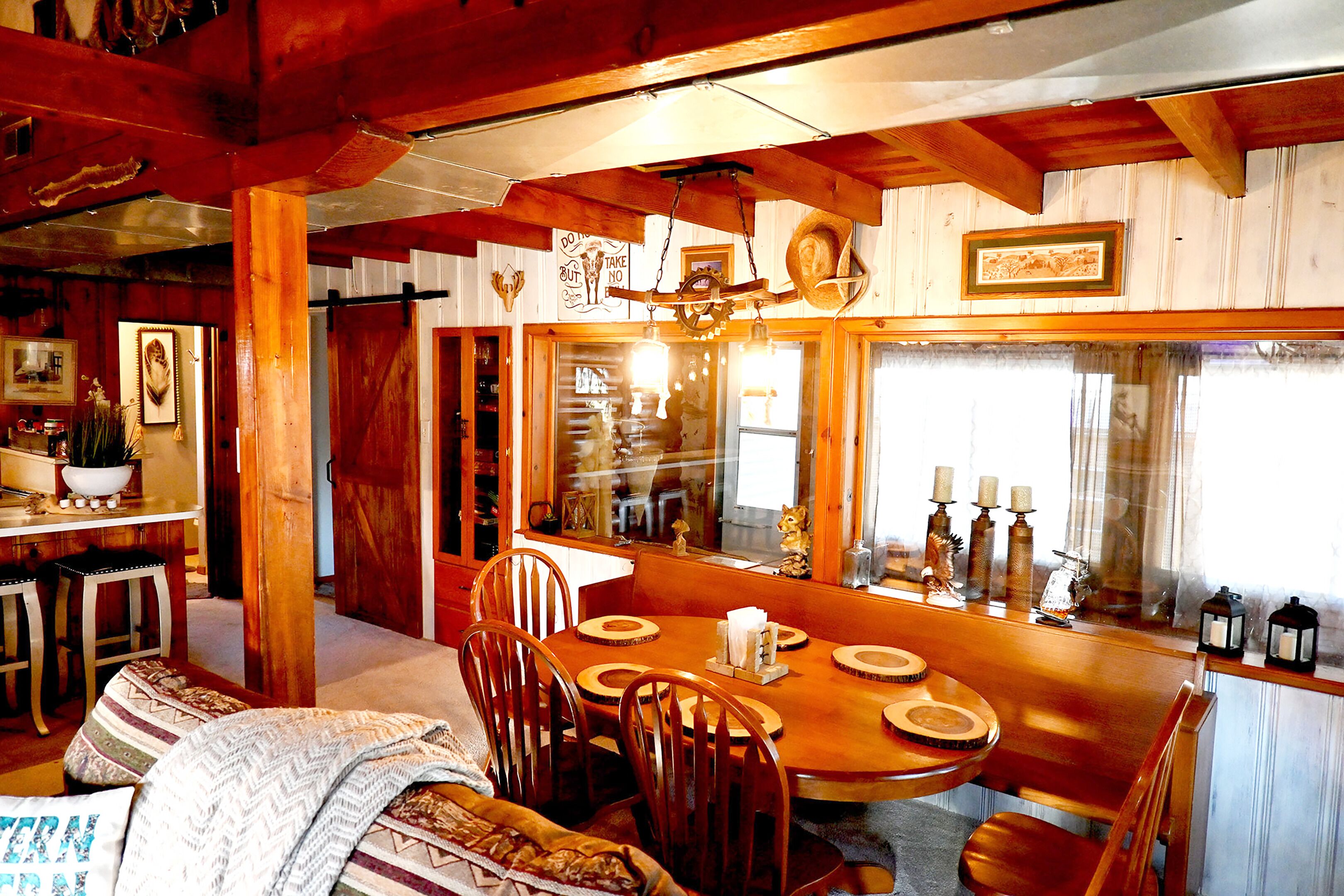 A cozy dining area with wooden furniture, a chandelier, and a large window with curtains.