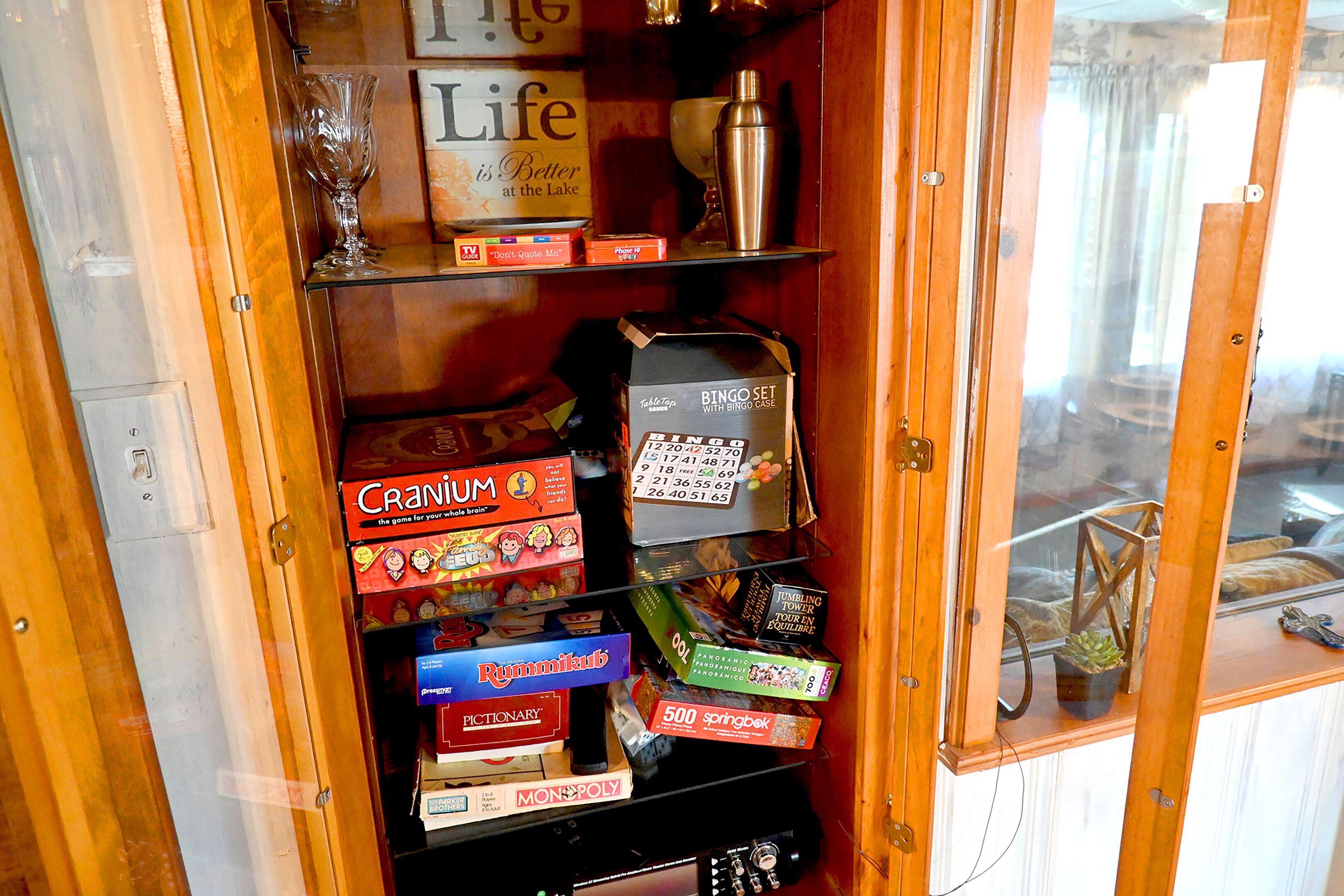 A wooden cabinet with shelves containing various board games, including Monopoly and Pictionary.