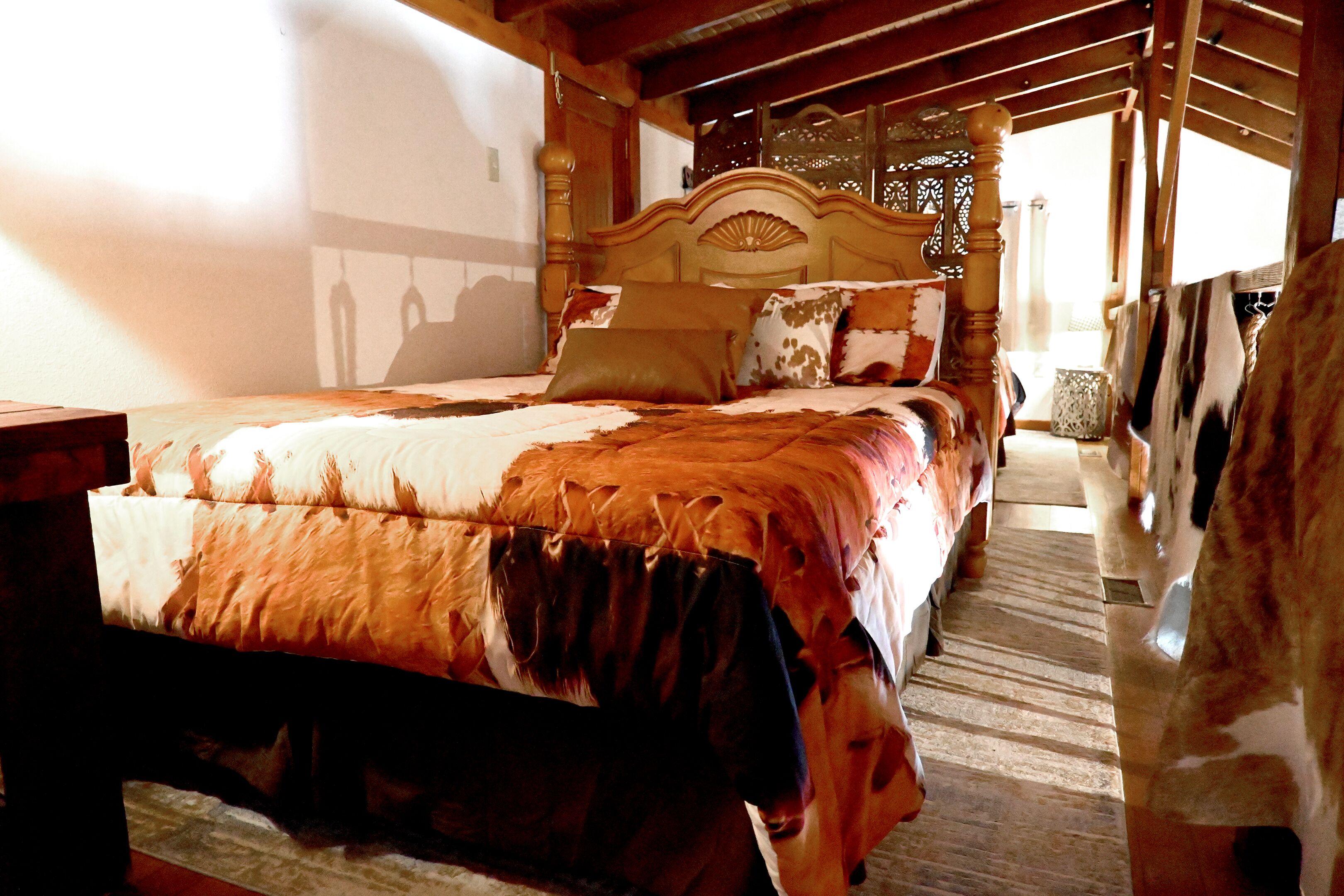 A bedroom with a wooden bed, a patterned bedspread, and a view of the outdoors.