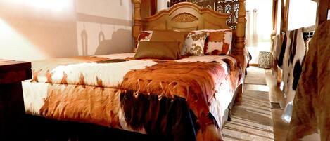 A bedroom with a wooden bed, a patterned bedspread, and a view of the outdoors.