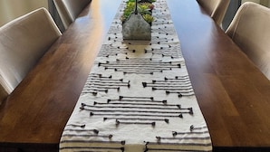 A dining table with a patterned tablecloth, surrounded by chairs, set against a backdrop of a clear sky and a mountainous landscape.