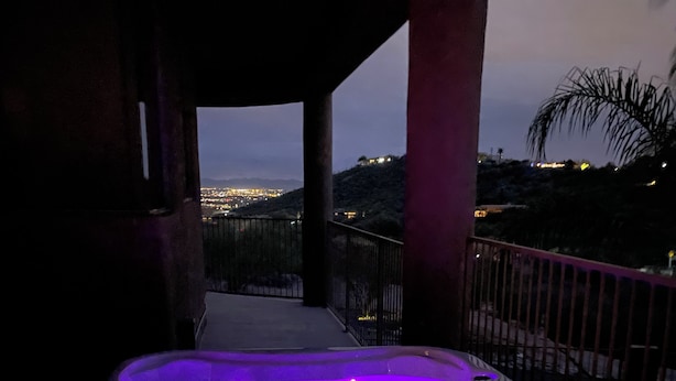 A hot tub with a digital control panel, surrounded by a balcony with a view of a cityscape at dusk.
