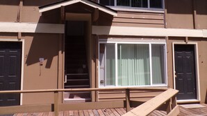 A two-story building with a wooden deck, a covered entrance, and a large window.