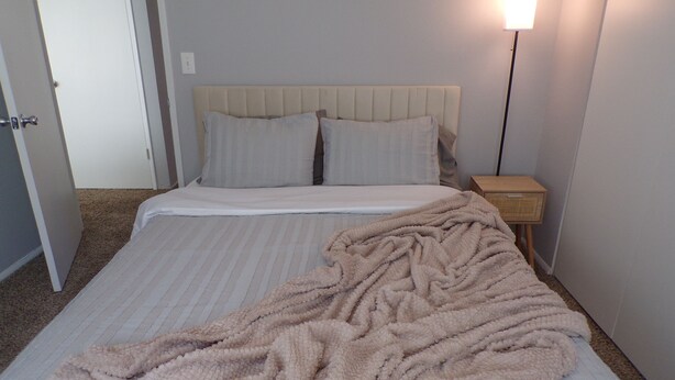 A bed with a striped bedspread and a beige blanket, a bedside table with a lamp, and a door in the background.
