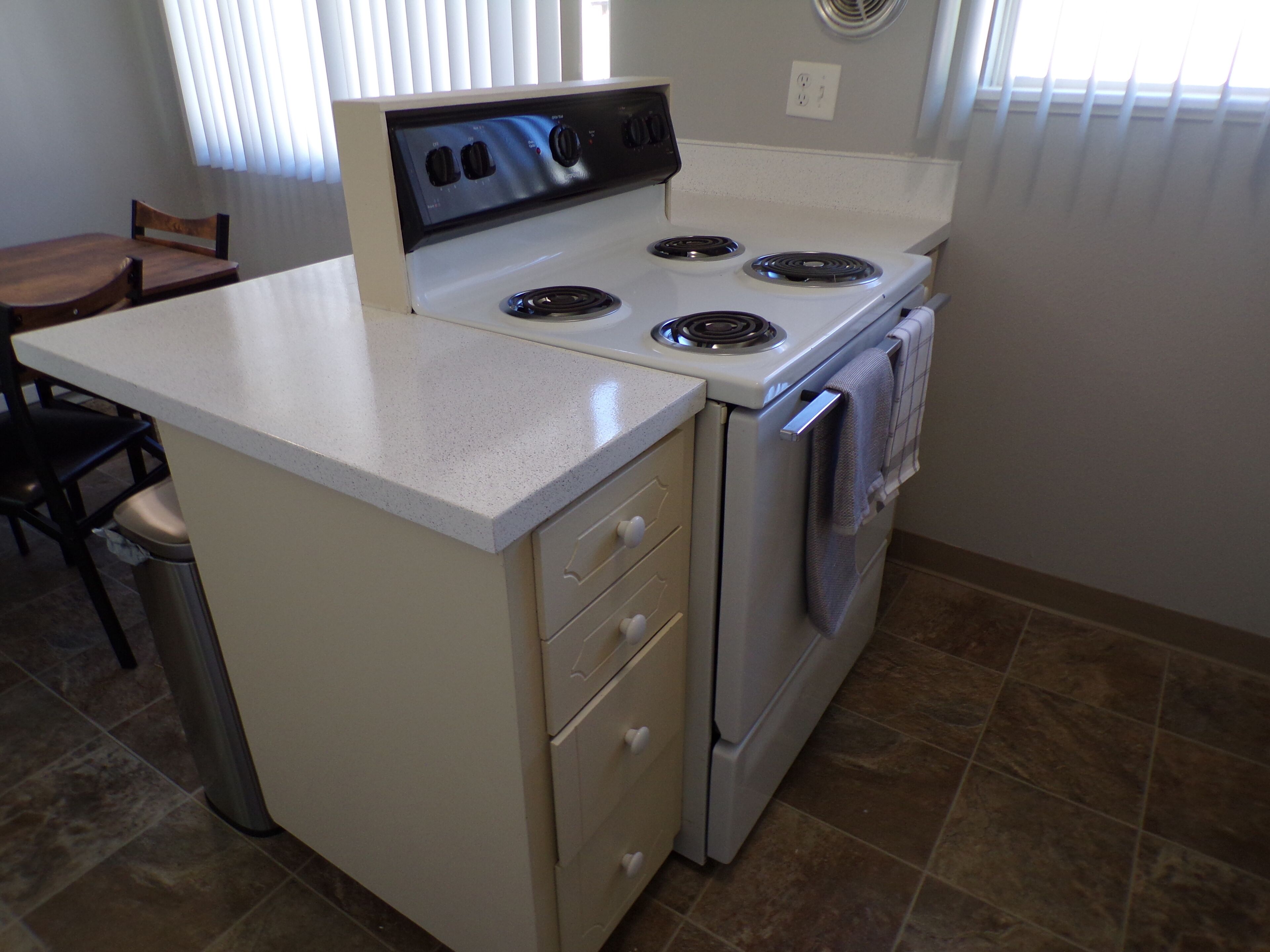 A compact kitchen with a stove, oven, and a small dining area with a chair.