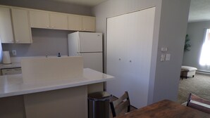 A compact kitchen with a white refrigerator, a sink, and cabinets. There is a wooden dining table with chairs.