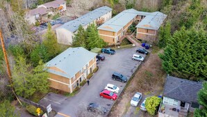An aerial view of a residential area with two multi-story buildings, a parking lot, and surrounding trees.