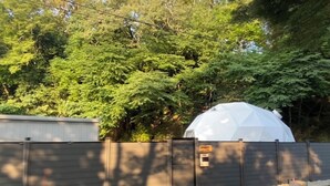 Une structure en forme de dôme blanc, entourée d’une clôture métallique, avec des arbres en arrière-plan.